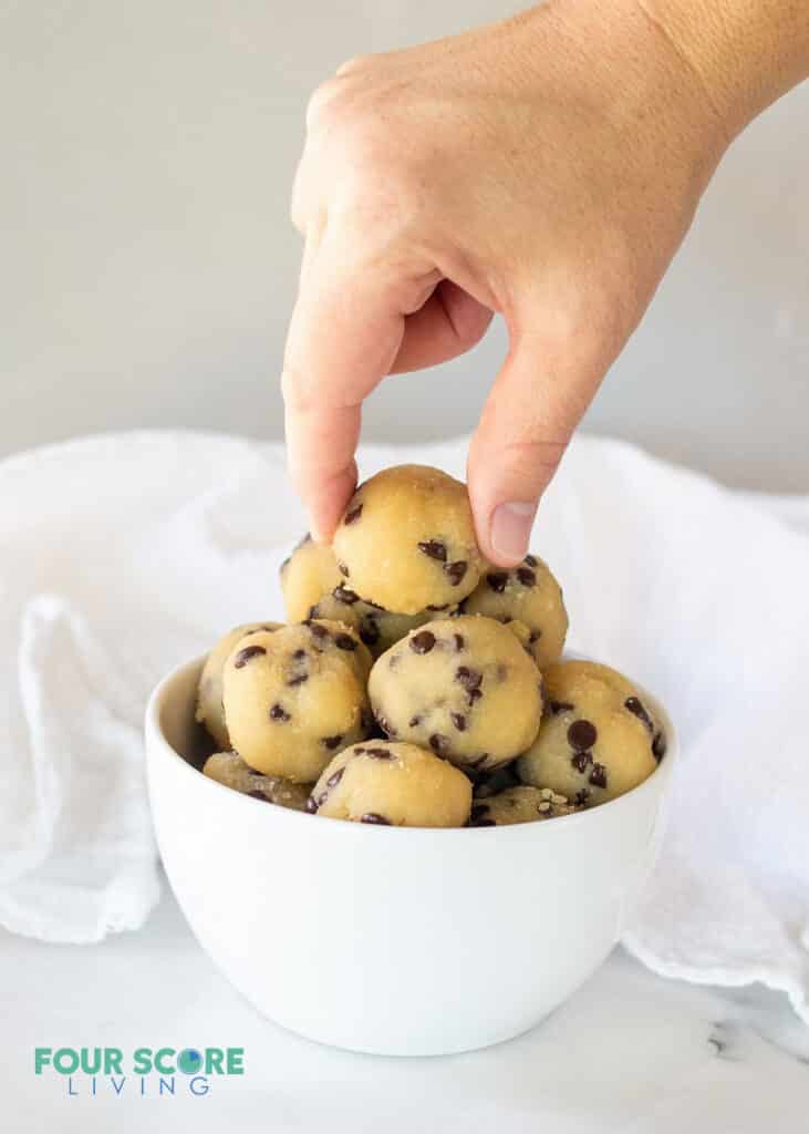a hand picking up a keto cookie dough bite from a white bowl