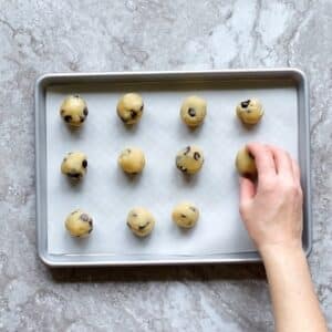 Top view photo of a sheet pan with parchment paper on it, and 12 Keto Cookie Dough balls on the sheet.