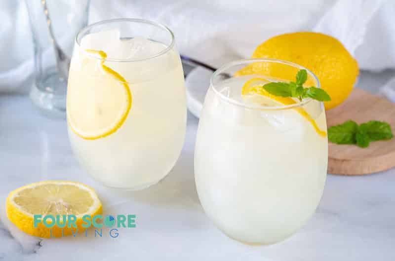 two glasses of keto lemonade with lemon and mint, with a lemon in the background