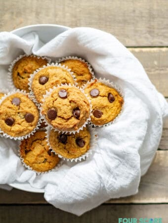 a close up of low carb pumpkin muffins with chocolate chips on a white dish towel in a bowl