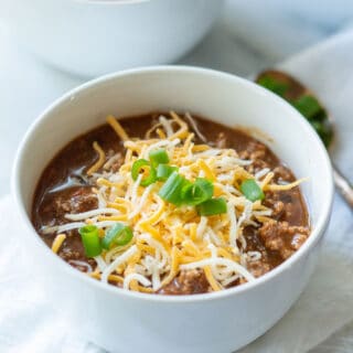 keto chili in a white bowl with cheese and green onions