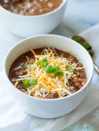 keto chili in a white bowl with cheese and green onions