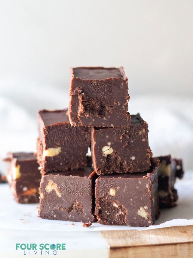 keto fudge stacked on white parchment paper that is layered over a wooden cutting board and a wooden surface. 