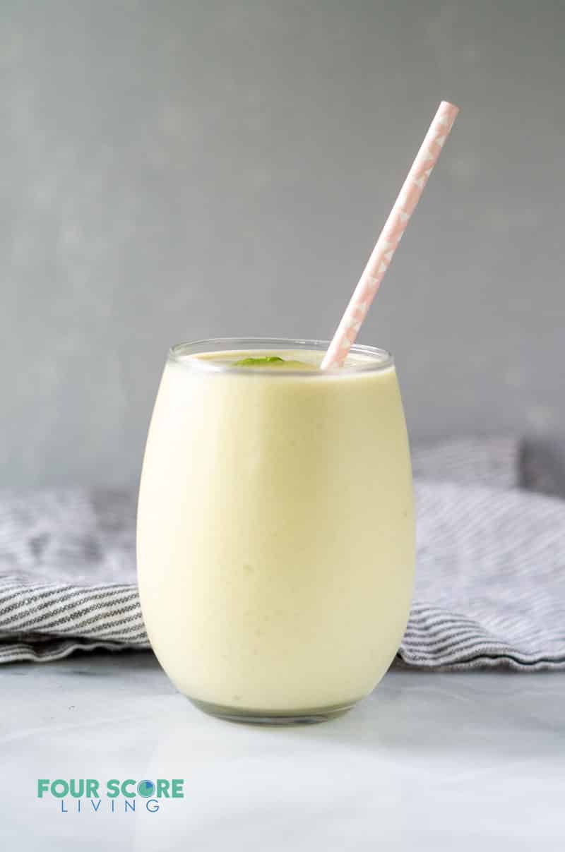 a cream colored smoothie in a glass with a pink straw in front of a gray background