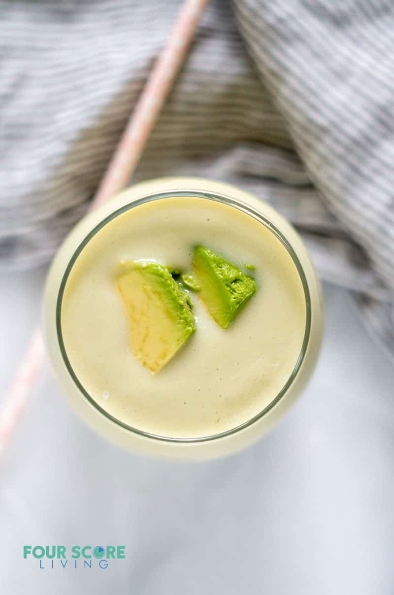 a glass filled with a cream colored beverage topped with a couple of fresh avocado pieces