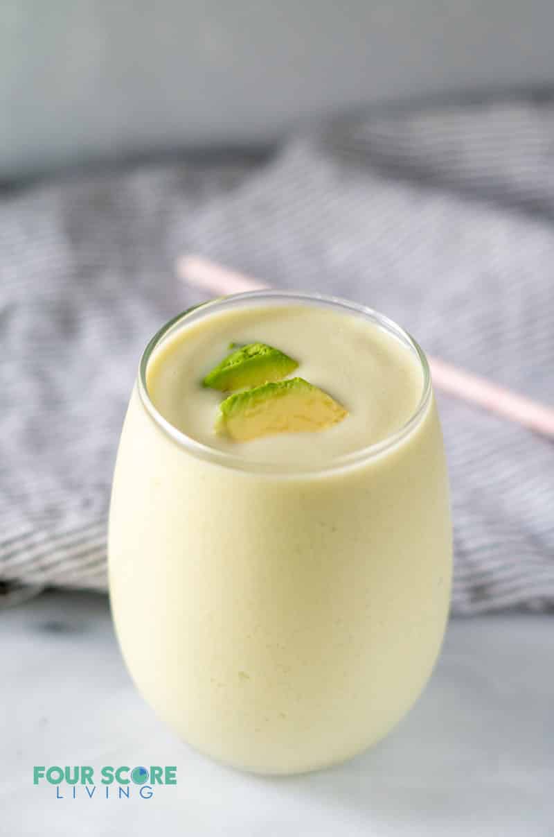 a creamy pale colored liquid inside a glass with pieces of fresh avocado as garnish