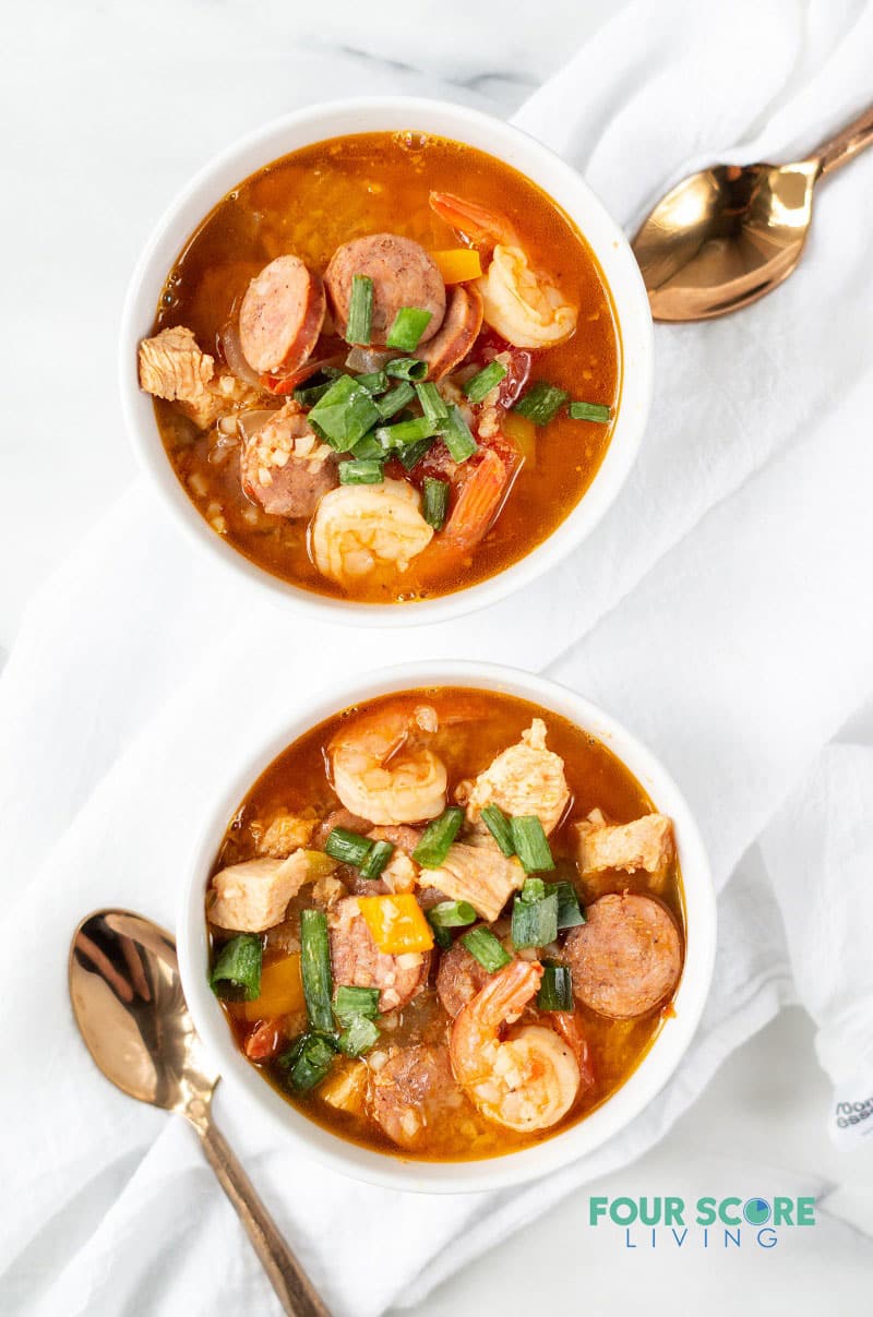 two white bowls filled with keto jambalaya in a red colored broth and topped with green herbs