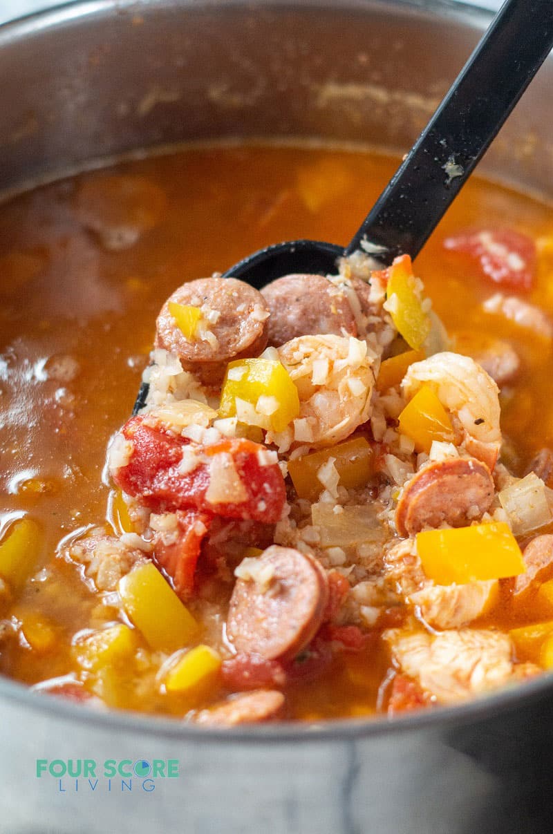a ladle scooping jambalaya with meat and veggies out of a large stock pot
