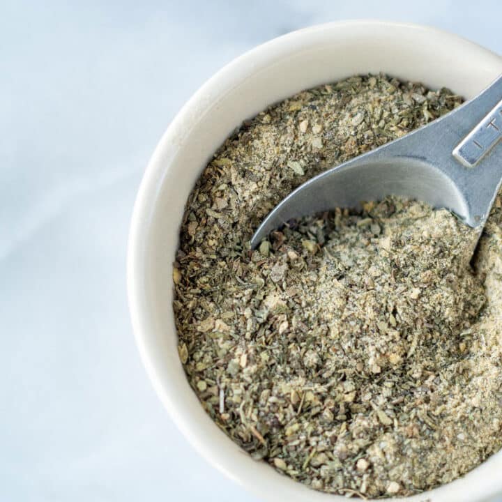 a measuring spoon scooping into a round white bowl of a greenish seasoning mix