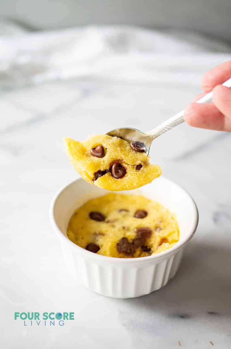 a spoon lifting a scoop of a keto chocolate chip mug cookie out of a white dish