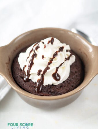 a chocolate mug cake with whipped cream and a drizzle of fudge in a brown ramekin