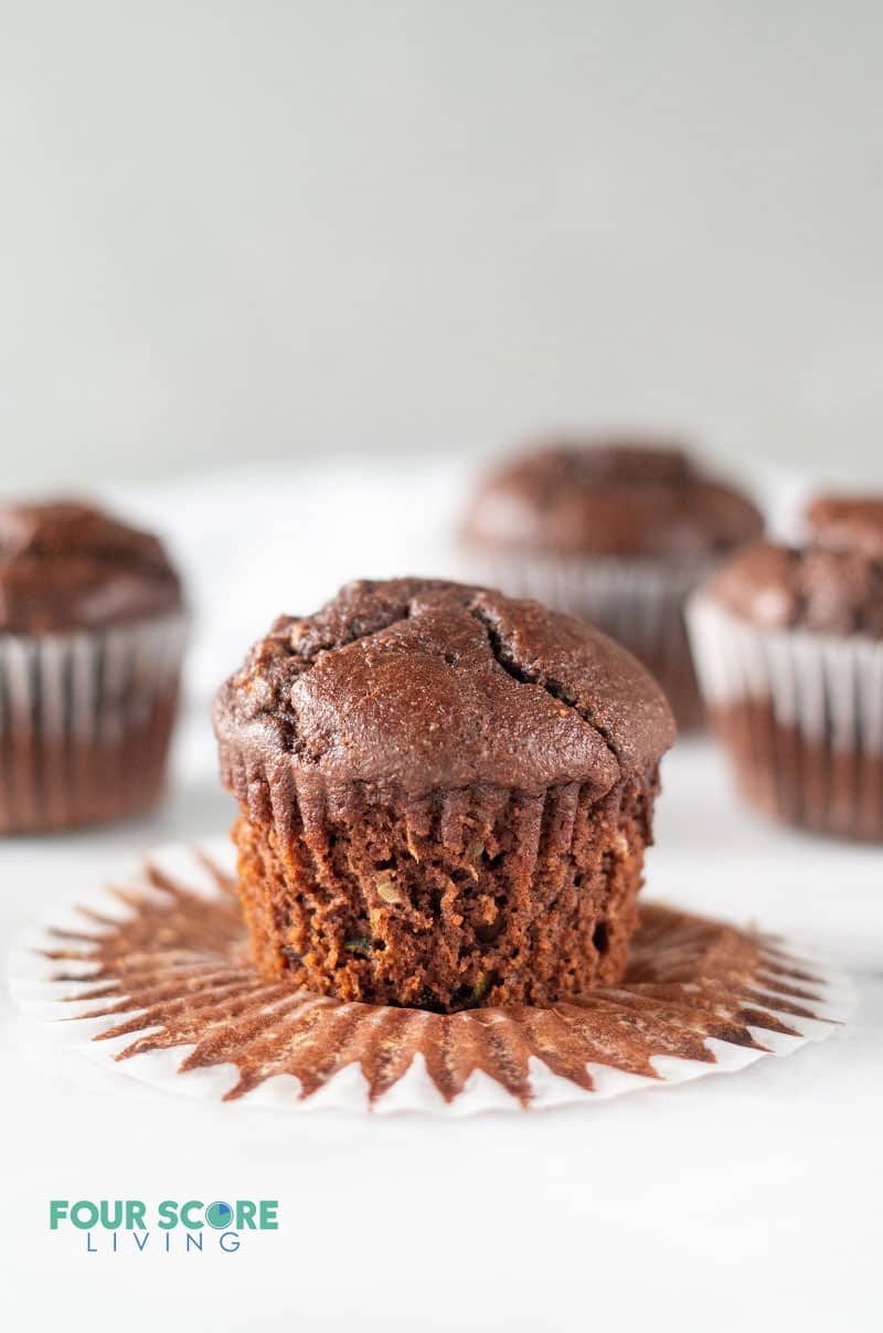 a chocolate muffin sitting on an open cupcake wrapper with several more chocolate muffins in the background