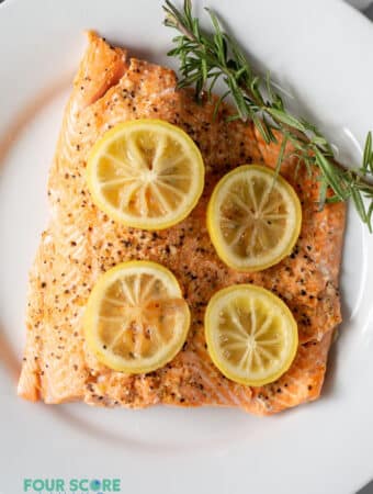 a cooked fillet of salmon topped with lemon slices and a sprig of fresh herbs