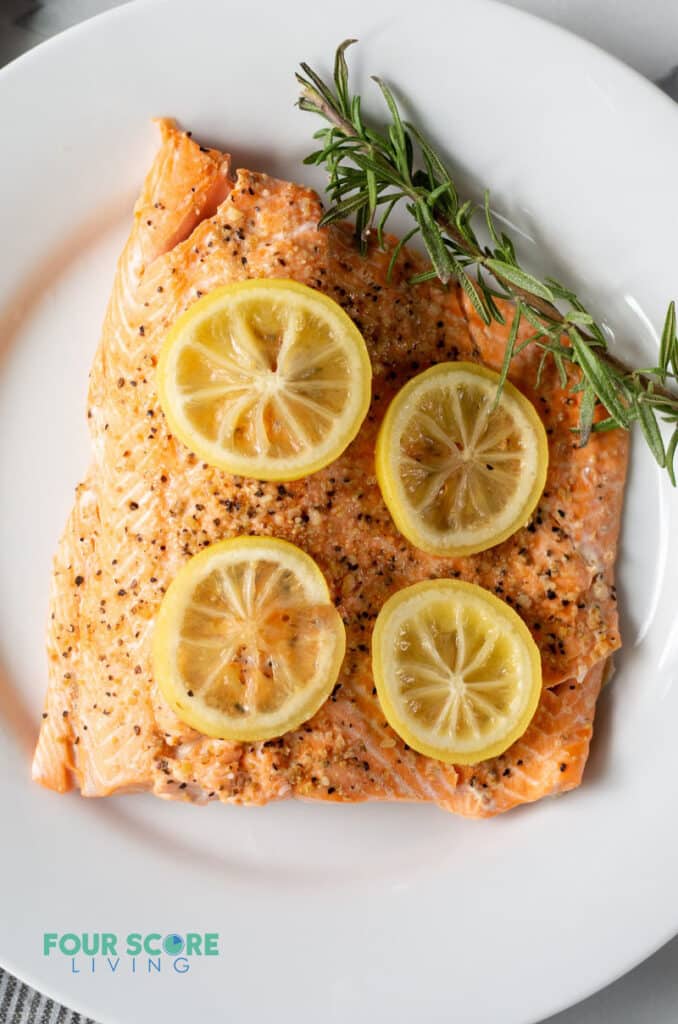 a cooked fillet of salmon topped with lemon slices and a sprig of fresh herbs
