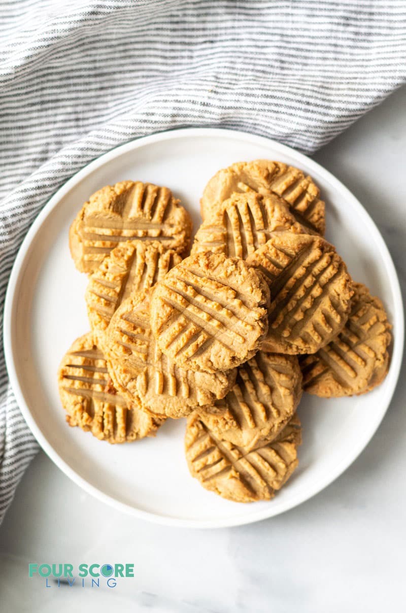 a stack of keto peanut butter cookies on a round white plate over a gray dish towel