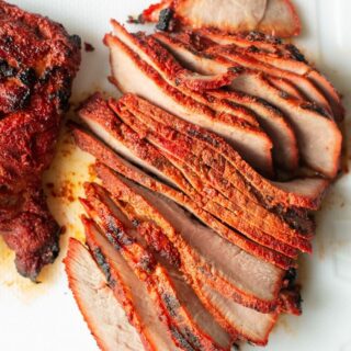 a slab of spiced cooked carne asada pork sliced into thin cuts on a white background