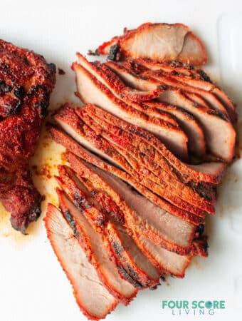 a slab of spiced cooked carne asada pork sliced into thin cuts on a white background