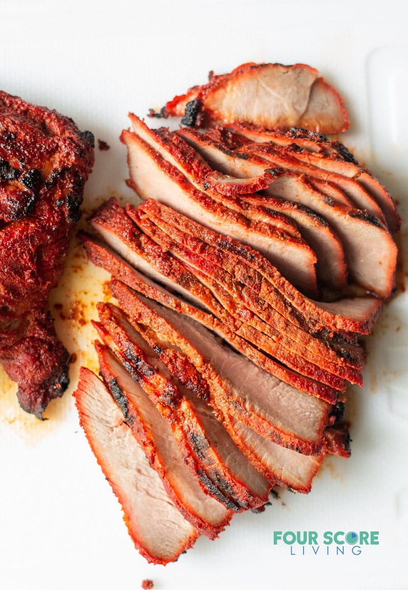 a slab of spiced cooked carne asada pork sliced into thin cuts on a white background