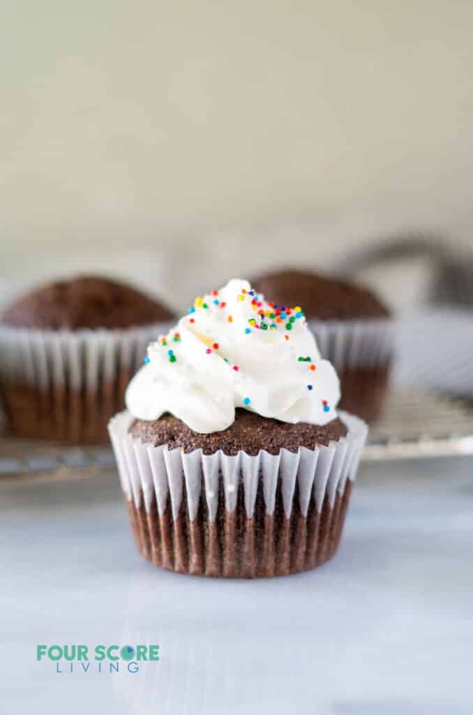 a almond flour chocolate cupcake in a white paper liner with whipped cream and sprinkles on top