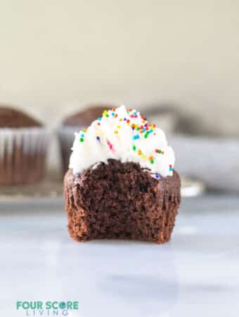 a keto chocolate cupcake with a bite out with whipped cream and sprinkles on top