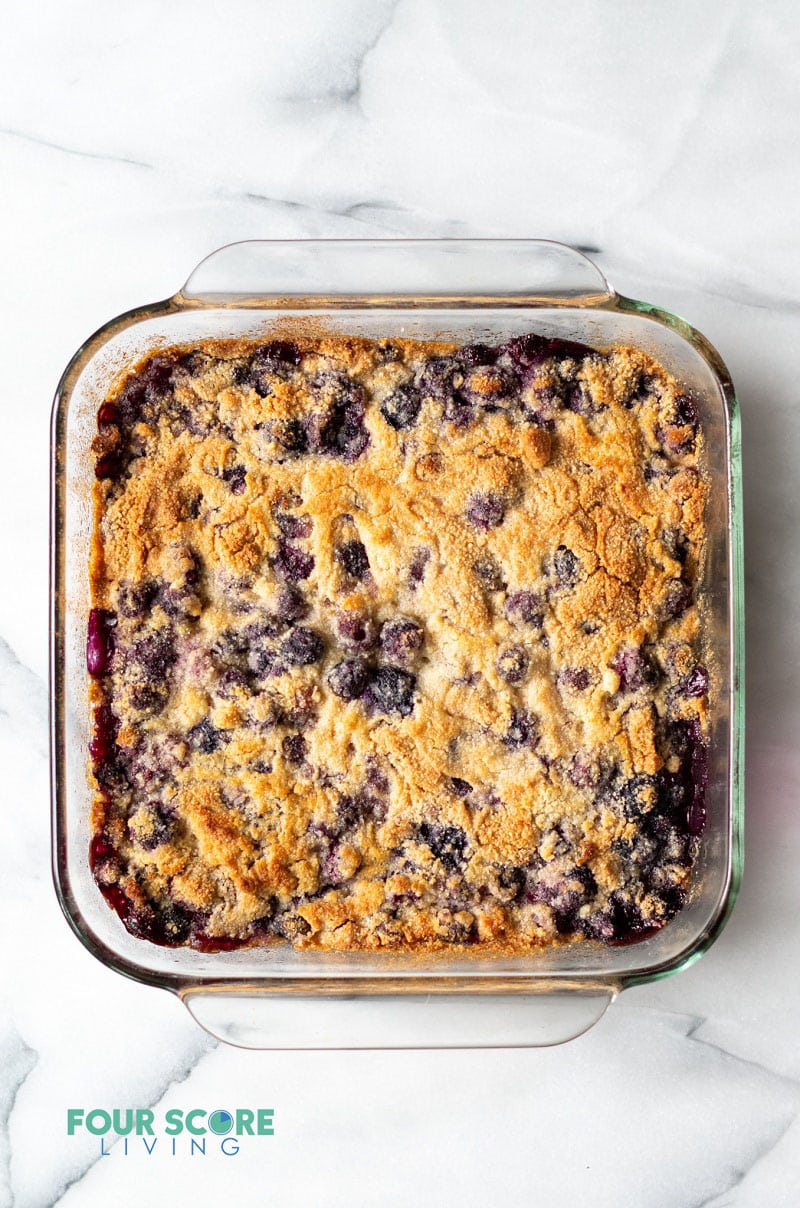 a clear square pan filled with a browned cake studded with blueberries