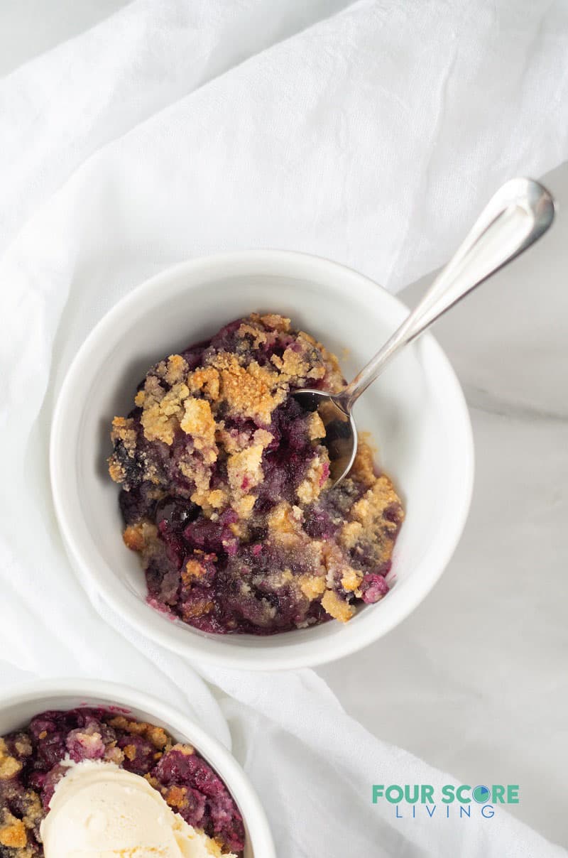 a small white bowl of blueberry dump cake with a spoon