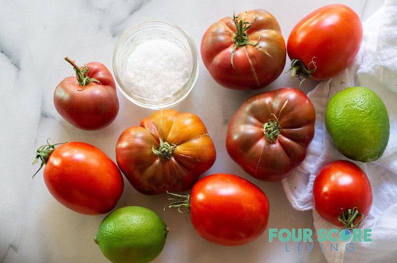 a variety of tomatoes with a bowl of salt and two limes