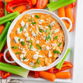 keto buffalo dip in a white bowl topped with blue cheese and onions