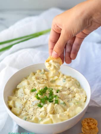 a hand dipping a cheese crisp into keto egg salad to show the texture