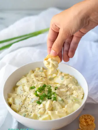 a hand dipping a cheese crisp into keto egg salad to show the texture