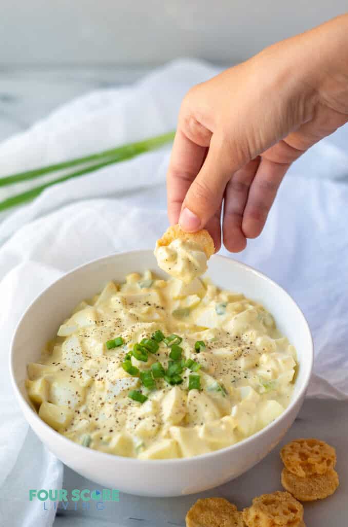 a hand dipping a cheese crisp into keto egg salad to show the texture