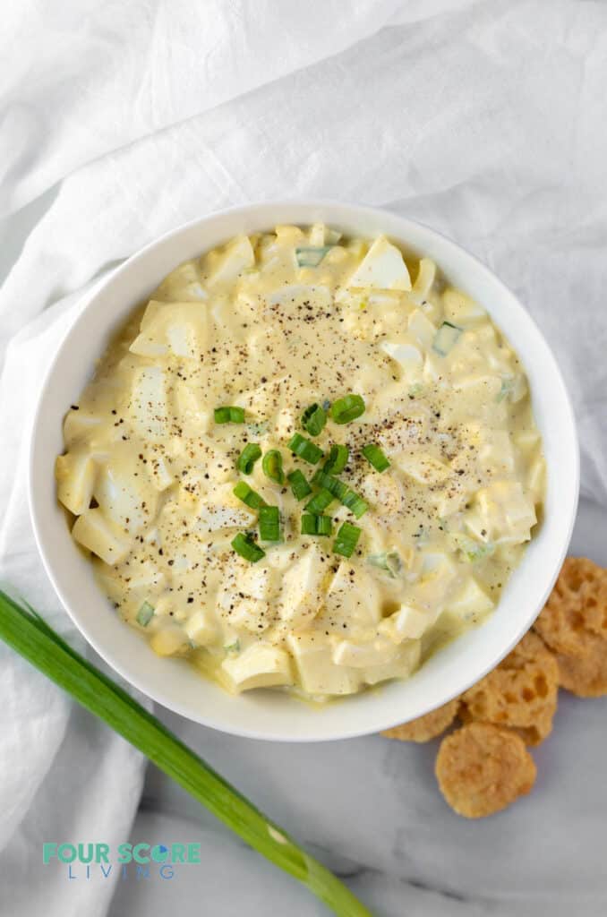 keto egg salad in a white bowl topped with sliced green onions and pepper