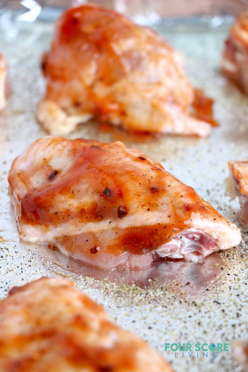 Raw chicken wings on a sheet pan, topped with bbq sauce.