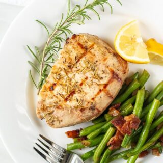 pork chop on a plate served with green beans, lemon wedges, and a rosemary garnish.