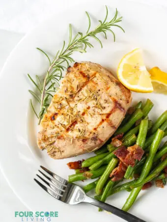 pork chop on a plate served with green beans, lemon wedges, and a rosemary garnish.