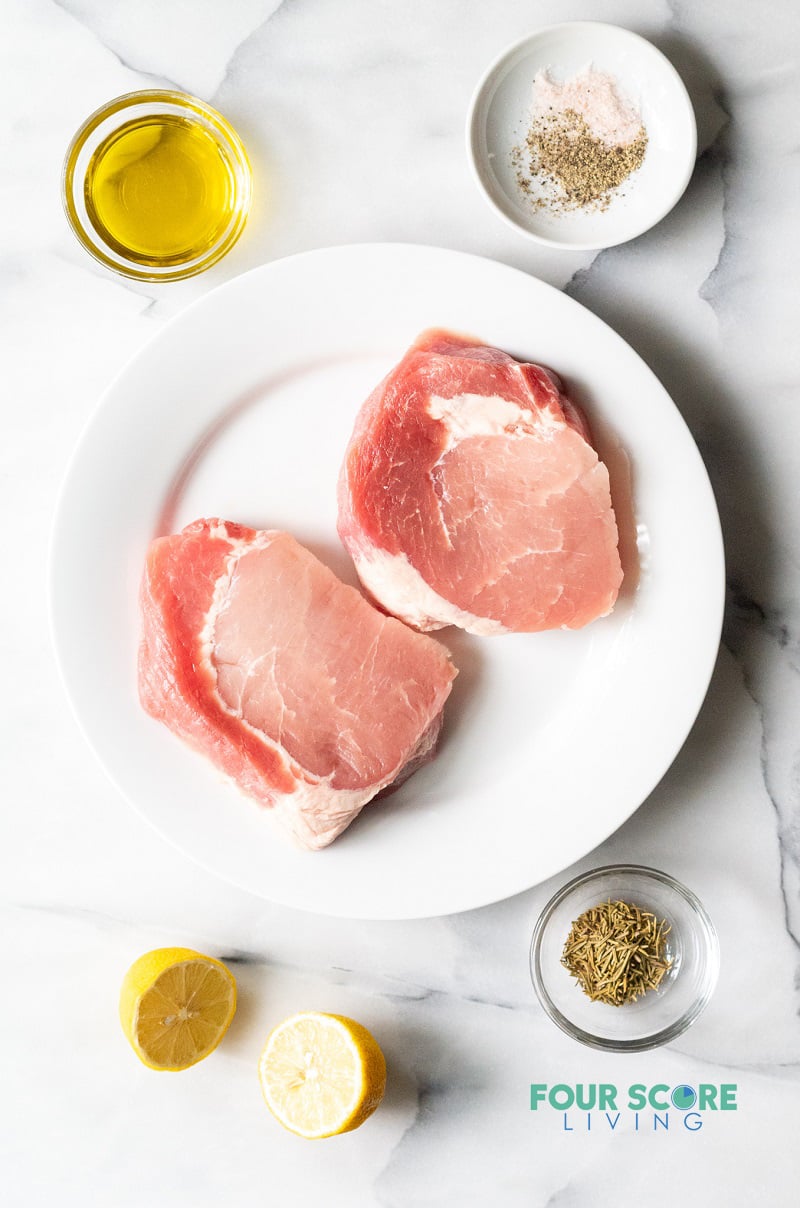 Raw pork chops on a plate with marinade ingredients in separate bowls