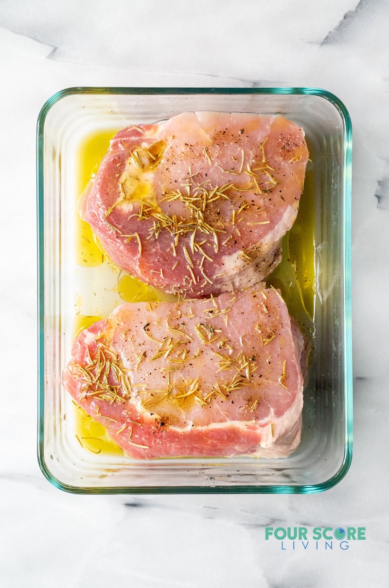 raw pork chops in a rectangular glass dish topped with marinade.