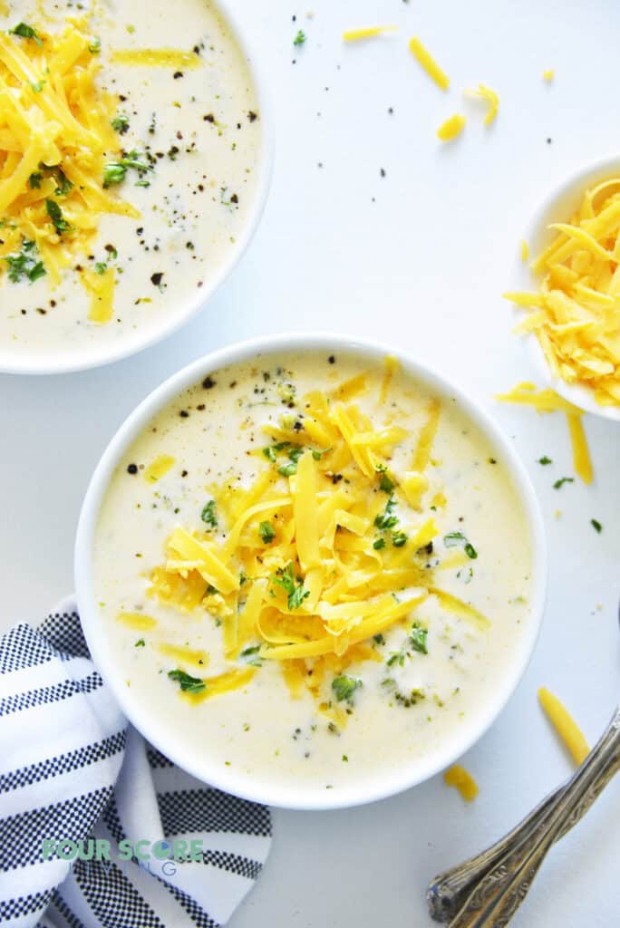 Top down view of a bowl of creamy broccoli cheese soup topped with cheddar cheese.