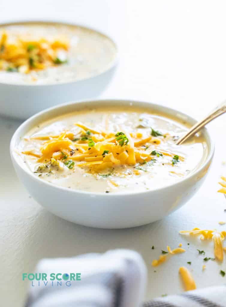 Side view of a bowl of broccoli cheese soup, topped with cheddar cheese.