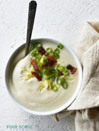 a bowl of creamy cauliflower soup topped with bacon and green onion