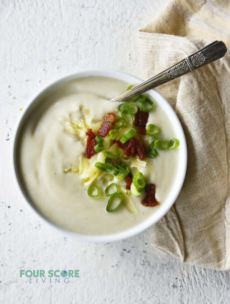 a bowl of cauliflower soup topped with onion, bacon and cheese.
