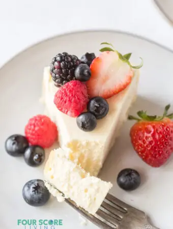 a slice of cheesecake on a plate, topped with fresh berries with a bite being taken.