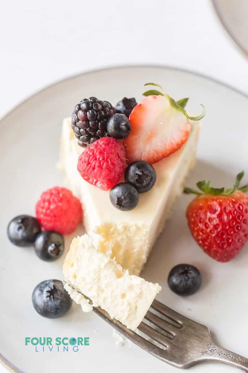 a slice of cheesecake on a plate, topped with fresh berries with a bite being taken.