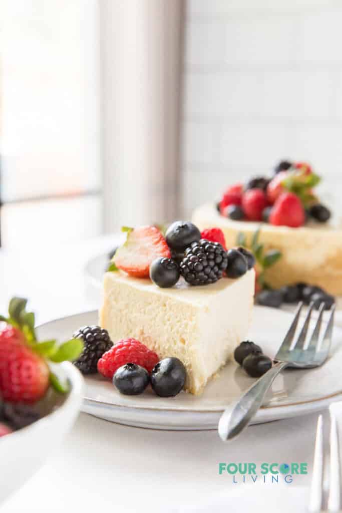 a slice of cheesecake topped with fresh berries. the rest of the cheesecake is in the background.