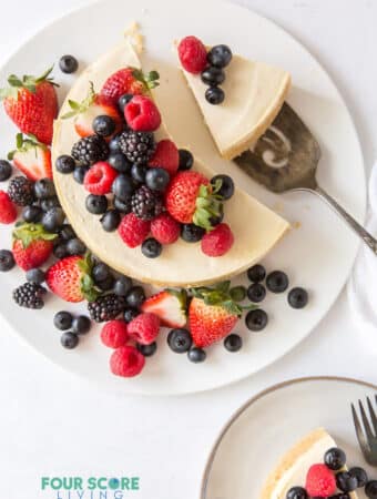 top down view of cheesecake topped with fresh berries. One slice is on a plate, another slice is being served.