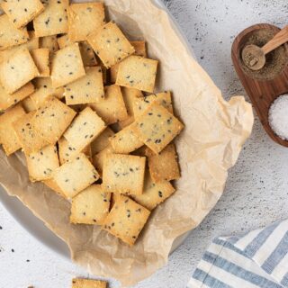 An oval dish lined with paper with square crackers inside.