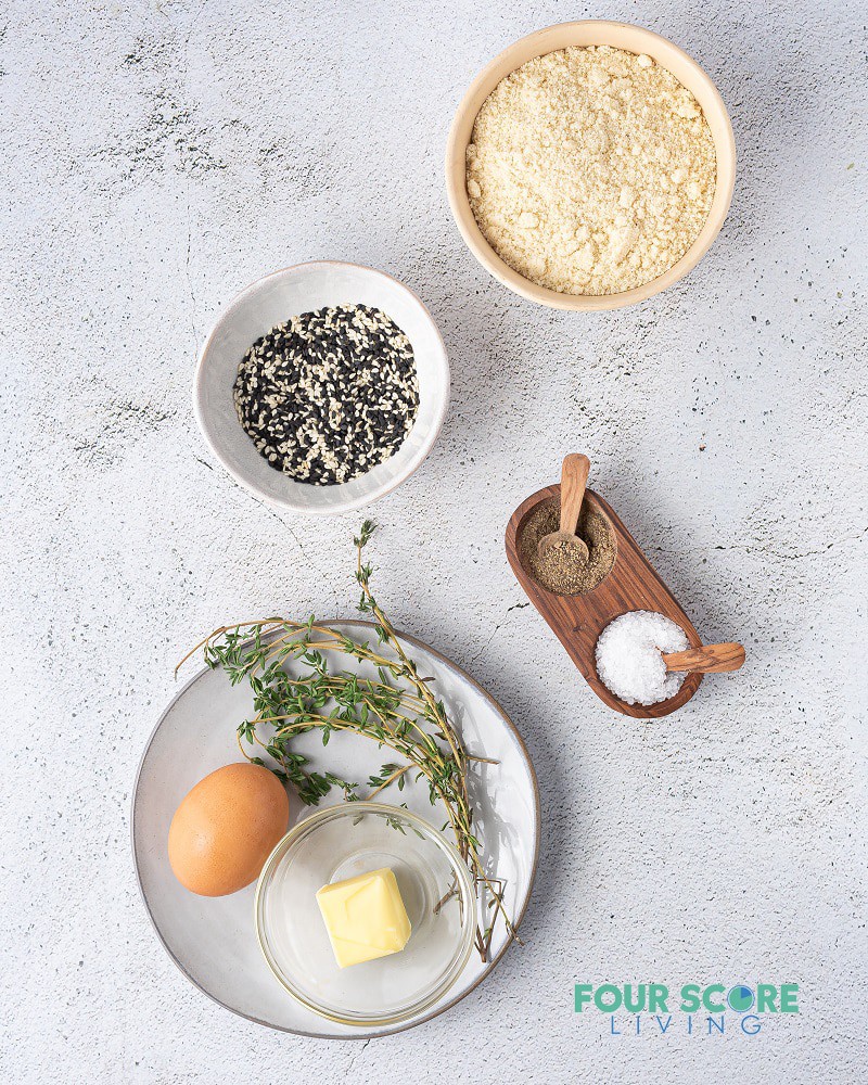 ingredients for keto crackers in separate dishes, including flour, seeds, egg, butter, and seasonings