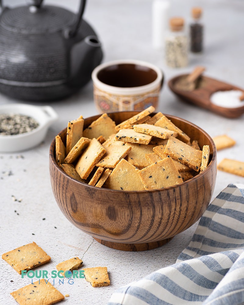 a wooden bowl full of square crackers being served with tea.