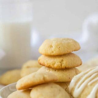 a stack of cream cheese cookies on a plate next to a glass of milk.