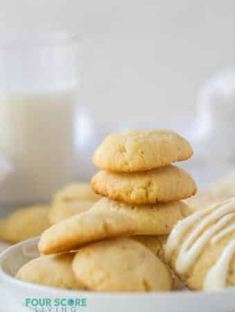 a stack of cream cheese cookies on a plate next to a glass of milk.